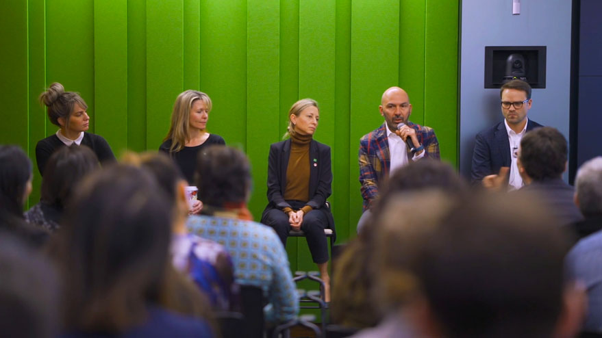 Group of employees sitting on a panel speaking to a crowd. 